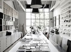 a long table with lots of books on it in front of large windows and shelves