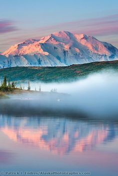 the mountains are covered in snow and mist as it sits on top of a body of water