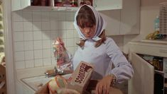 a woman in a white hoodie is preparing food on the kitchen counter and looking down