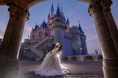 a bride and groom kissing in front of a castle at dusk with the sun setting