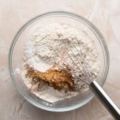 a glass bowl filled with dry ingredients next to a whisk on a table