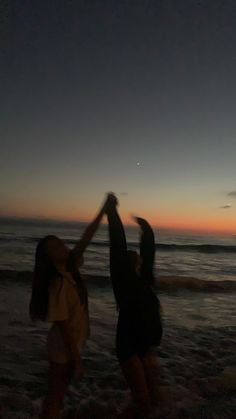 two girls are playing on the beach at sunset with their arms up in the air