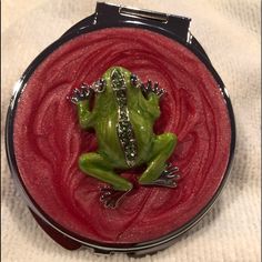 a green frog sitting on top of a red substance in a metal container with silver flecks