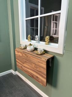 a wooden cabinet with two bowls on it in front of a window that is painted green