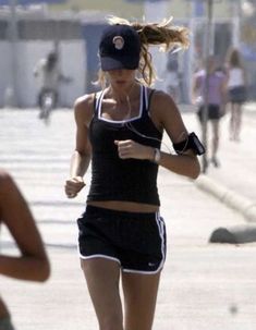 a woman running down the street in shorts and a tank top with her hat on