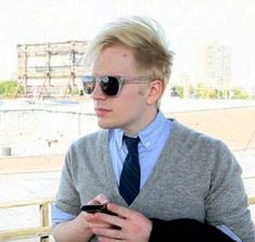 a man with sunglasses and a tie is looking at his cell phone