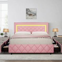 a pink bed with drawers underneath it in a white walled room next to two lamps