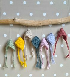 five crocheted hats hanging from a wooden stick on a polka dot tablecloth