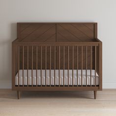 a wooden crib with white bedding and wood flooring in an empty room