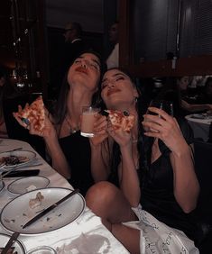 two women sitting at a table eating pizza