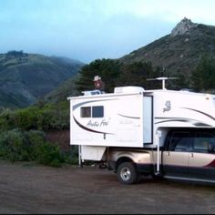 an rv parked on the side of a road with mountains in the backgroud