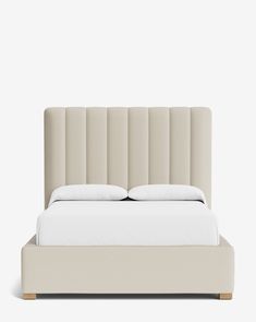 an upholstered bed with white sheets and pillows