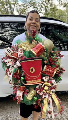 a woman standing in front of a white car holding a christmas wreath with presents on it