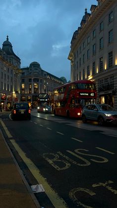 a city street filled with lots of traffic next to tall buildings at night, lit up by lights