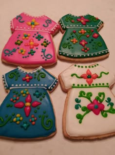 four decorated cookies in the shape of dresses on a white tablecloth with pink, blue and green frosting