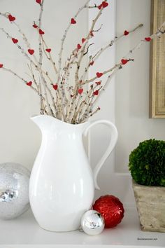 a white vase filled with branches and red berries on top of a table next to ornaments