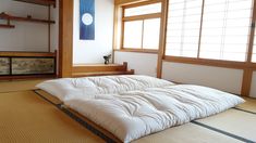 a bed sitting in the middle of a room next to two wooden shelves and windows