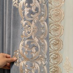 a hand is holding the curtain in front of two curtains with gold and silver designs on them