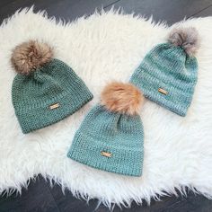 two knitted hats with pom - poms laying on top of a white rug