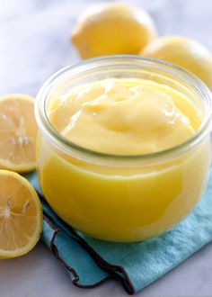 a glass jar filled with lemon custard on top of a blue towel next to sliced lemons