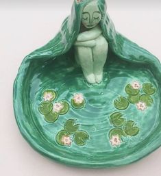 a ceramic figurine sitting on top of a bowl filled with water lilies