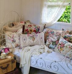 a white bed with lots of pillows on top of it next to a dresser and window