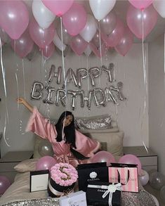 a woman sitting on top of a bed surrounded by pink and white balloons, presents and gifts