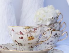 three tea cups and saucers sitting on a white table cloth with flowers in the background