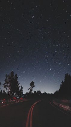 the night sky is filled with stars and cars driving on a road in front of some trees