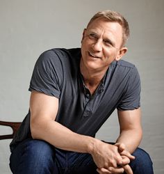 a man sitting on top of a wooden chair next to a white wall and smiling