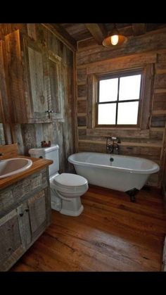 a bathroom with wooden walls and flooring has a bathtub, toilet, and sink