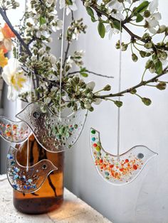 two glass birds hanging from a branch in front of a vase filled with flowers and beads