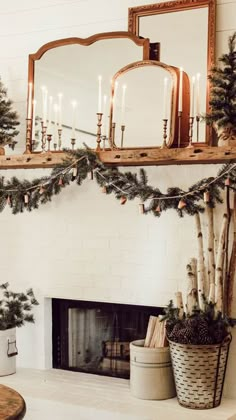 a fireplace decorated for christmas with candles and evergreen garland on the mantel above it