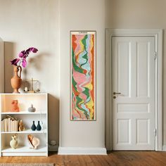 a painting hangs on the wall next to a bookshelf with vases and other items