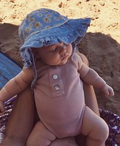 a baby wearing a blue hat laying on top of a beach towel in the sand