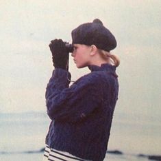 a woman standing on top of a beach next to the ocean wearing a hat and gloves