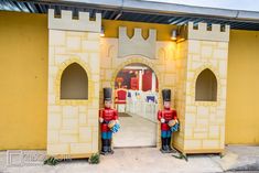 two toy soldiers are standing in front of a yellow wall with arches and archways