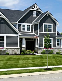 a large gray house with white trim on the front and side windows, grass in front