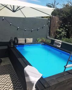 an outdoor swimming pool with lounge chairs and umbrellas around it, surrounded by greenery