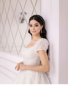 a woman in a white dress leaning against a wall with her hands on her hips