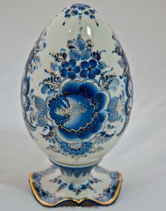 an egg shaped vase with blue flowers on it's side and gold trimmings