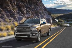 the front end of a silver ram truck driving down a road with mountains in the background