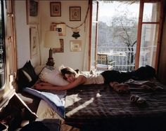 a woman laying on top of a bed in a bedroom next to a window with lots of windows