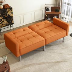 an orange couch sitting on top of a rug in a living room next to a window