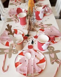 the table is set with pink and red plates, cups, spoons and forks