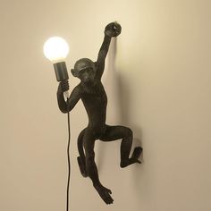 a monkey statue holding a light bulb up to it's head on a wall