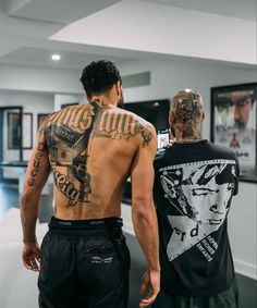 two men with tattoos on their back standing next to each other in front of a mirror