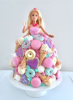 a barbie doll sitting on top of a cake covered in cookies and doughnuts