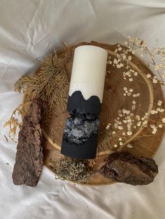 a white candle sitting on top of a wooden plate next to rocks and dried plants