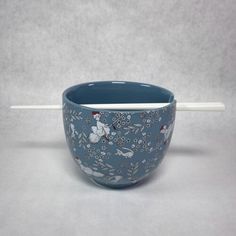 a blue bowl with white handles and flowers on the side, sitting on a gray surface